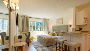 A modern hotel room with a bed, a small dining area, a sitting area with a chair, a TV, and a window with curtains. - Downtown Studio with King Bed & City Views (Seattle)