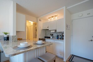 A compact kitchen with white cabinets, a granite countertop, and a built-in oven. - Downtown Studio with King Bed & City Views (Seattle)