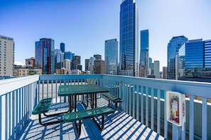 A rooftop terrace with a table and benches, overlooking a city skyline with modern buildings. - Downtown Studio with King Bed & City Views (Seattle)