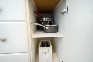 Pieni, käytännöllinen keittiö, jossa on valkoinen kaappi, leivänpaahdin ja pino kattiloita hyllyllä.