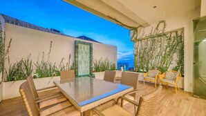 Un patio al aire libre con muebles de mimbre, una mesa de vidrio y vistas de la ciudad.