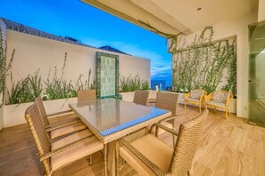An outdoor patio with wicker furniture, a glass table, and a view of the cityscape.