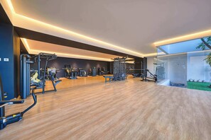 A modern gym with various exercise equipment, a wooden floor, and a large window offering a view of the outdoors.