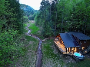 A cabin with a deck, a hot tub, and a river in the background.