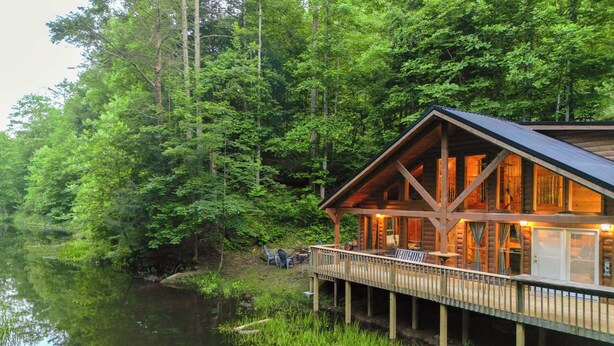 Une cabane dotée d’une terrasse, entourée d’une forêt dense et bordée d’un lac paisible.