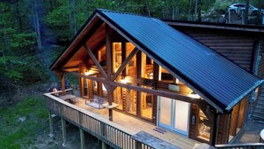 Une cabane en rondins dotée d’une terrasse, de grandes fenêtres et d’un foyer extérieur.