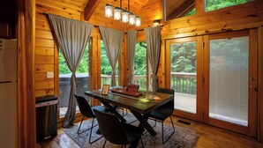 L’intérieur d’une cabane en bois, avec une table à manger, des chaises, un réfrigérateur et une poubelle.