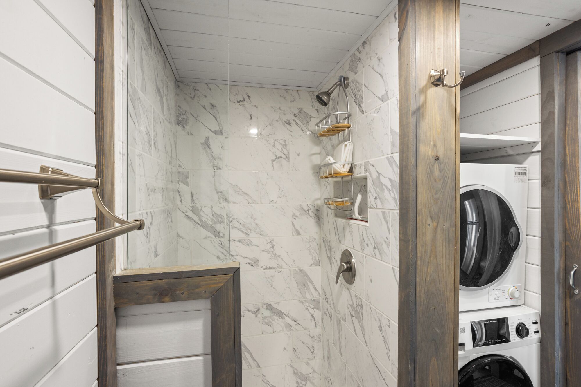 A compact laundry room with a built-in washer and dryer, marble-tiled walls, and a wooden-framed door.