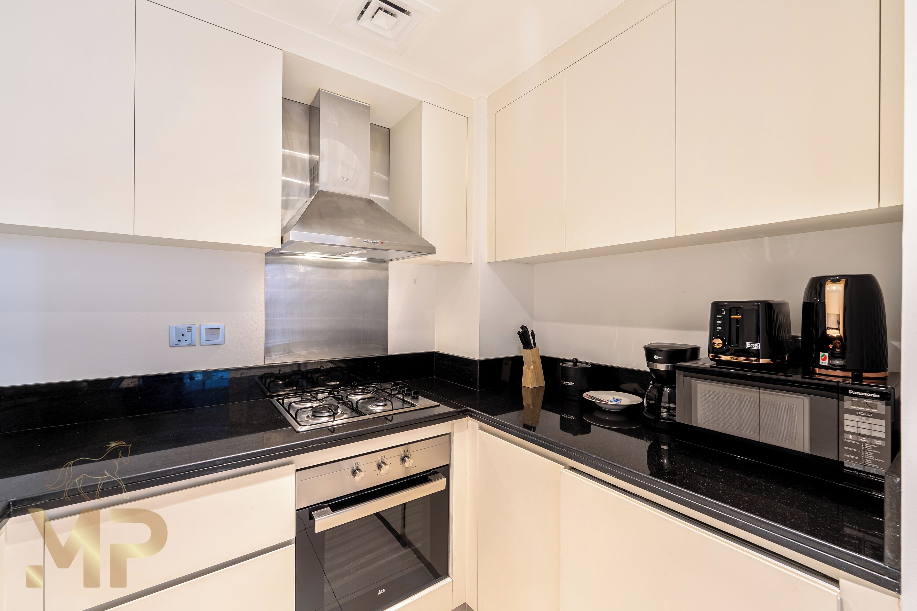 Una cocina moderna con armarios blancos, encimera negra, electrodomésticos de acero inoxidable y una cafetera.