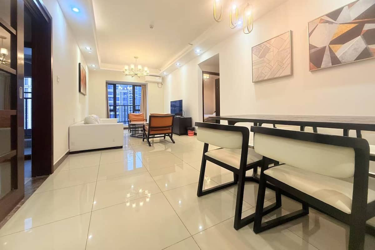 A modern living room with a white sofa, a dining table with chairs, a chandelier, and artwork on the walls.