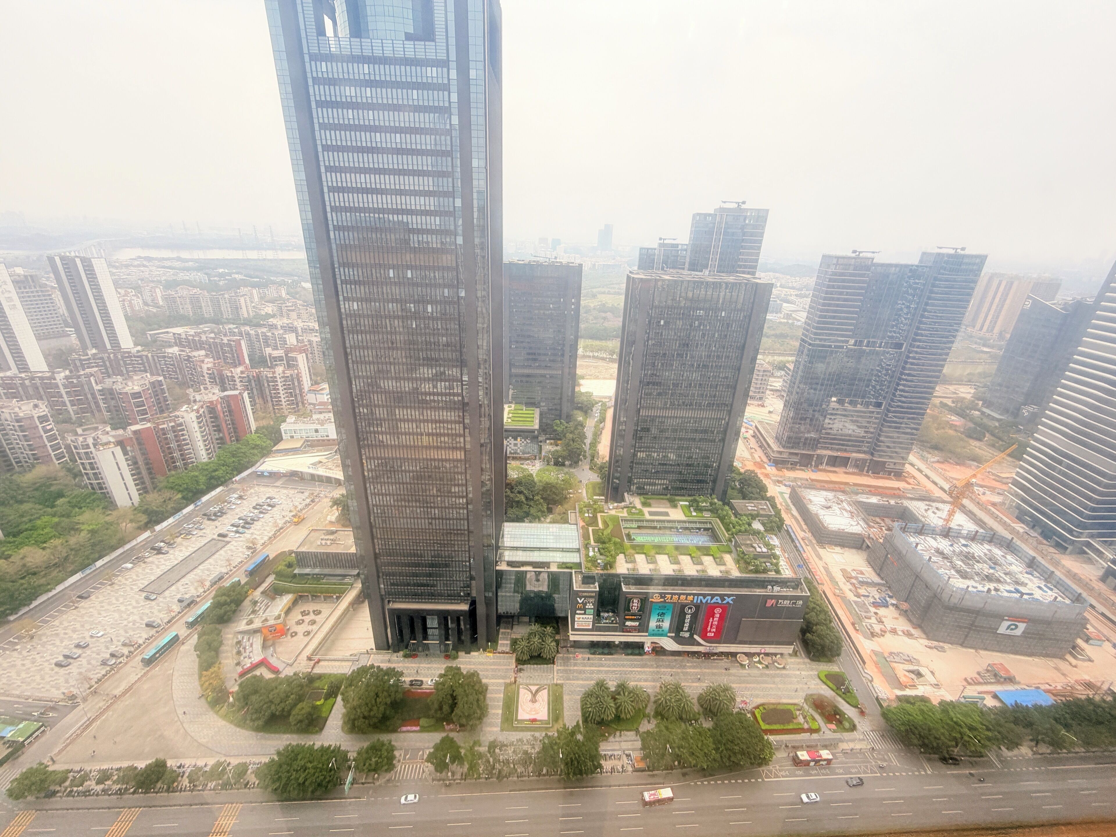 Un edificio de gran altura con fachada de vidrio moderna, rodeado de otros edificios altos y un estacionamiento.