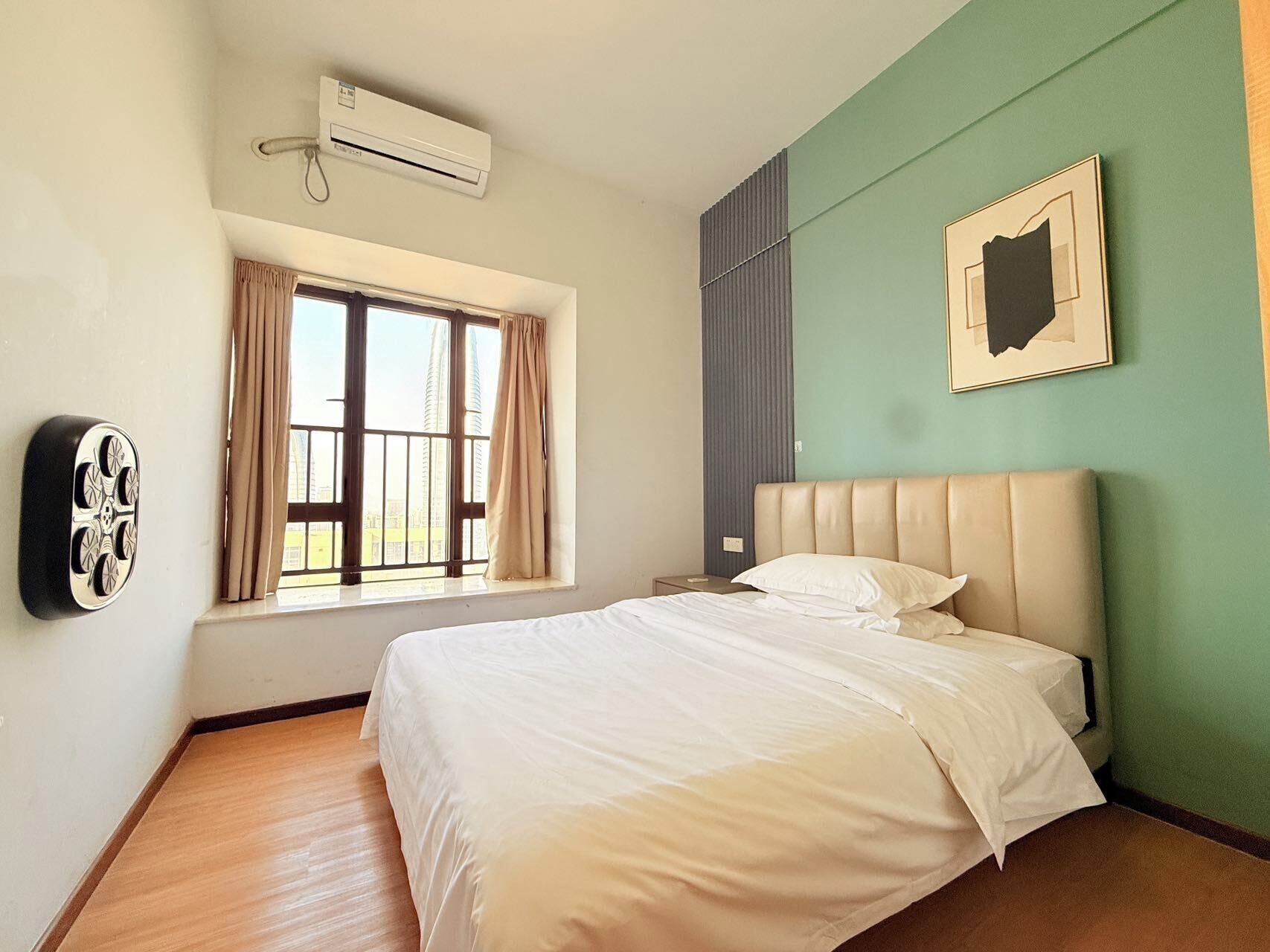 Ein Schlafzimmer mit Bett, einem Fenster mit Vorhängen, einer Klimaanlage, einem Wandbild und einem Nachttisch.