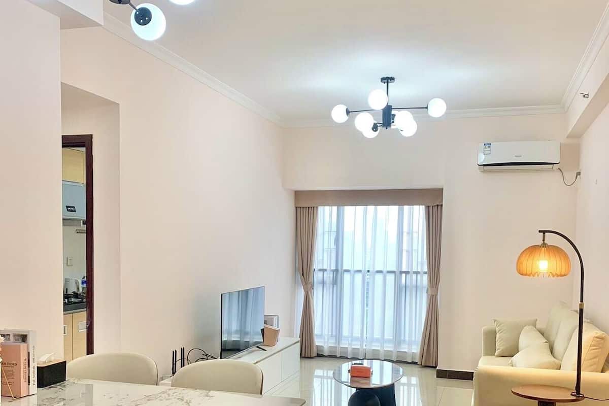 A modern living room with a marble dining table, a sofa, a coffee table, and a lamp. There is a TV and a window with curtains.