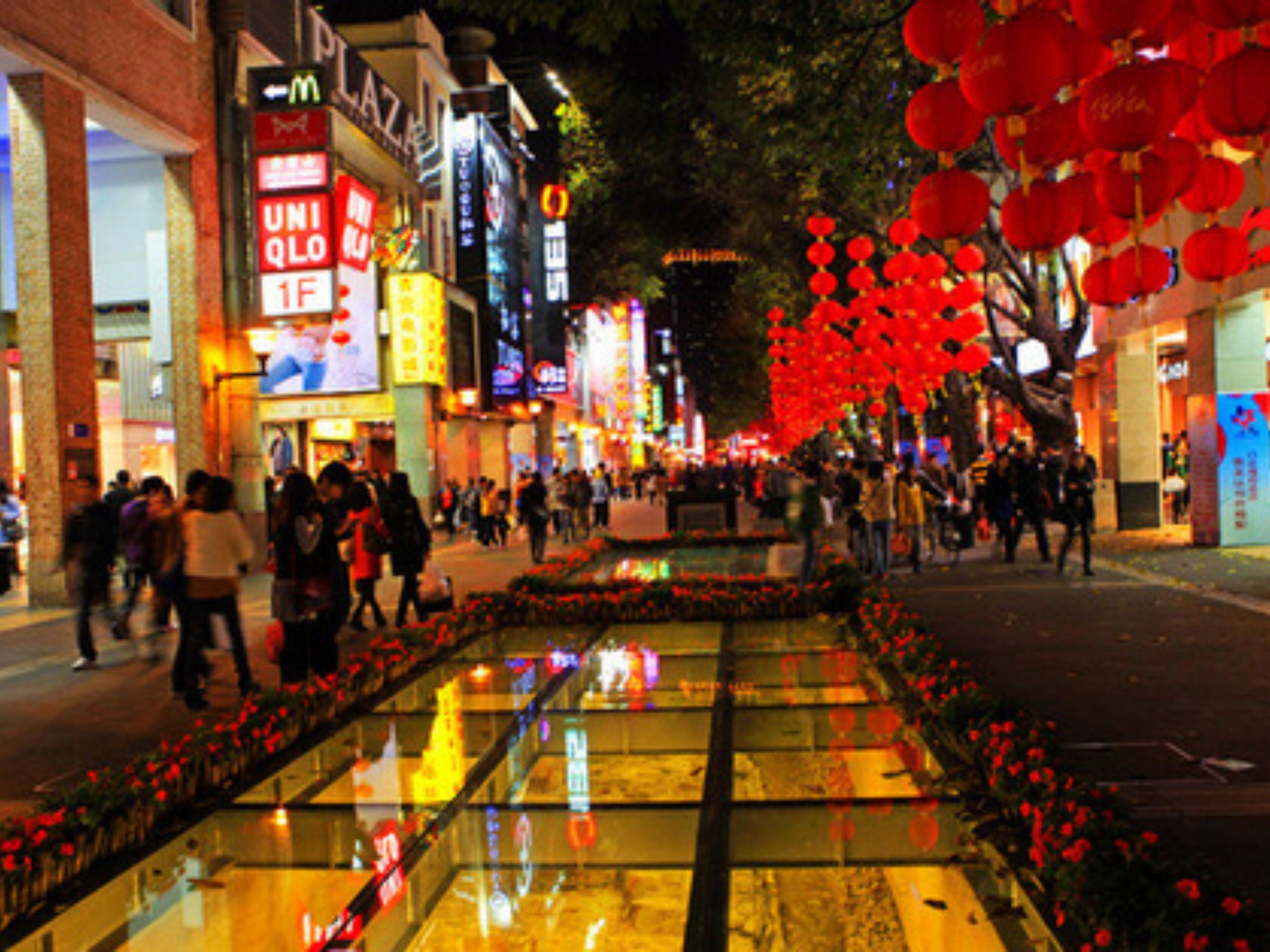 Une rue animée en milieu urbain, avec un trottoir pour les piétons, des boutiques et des lanternes rouges.