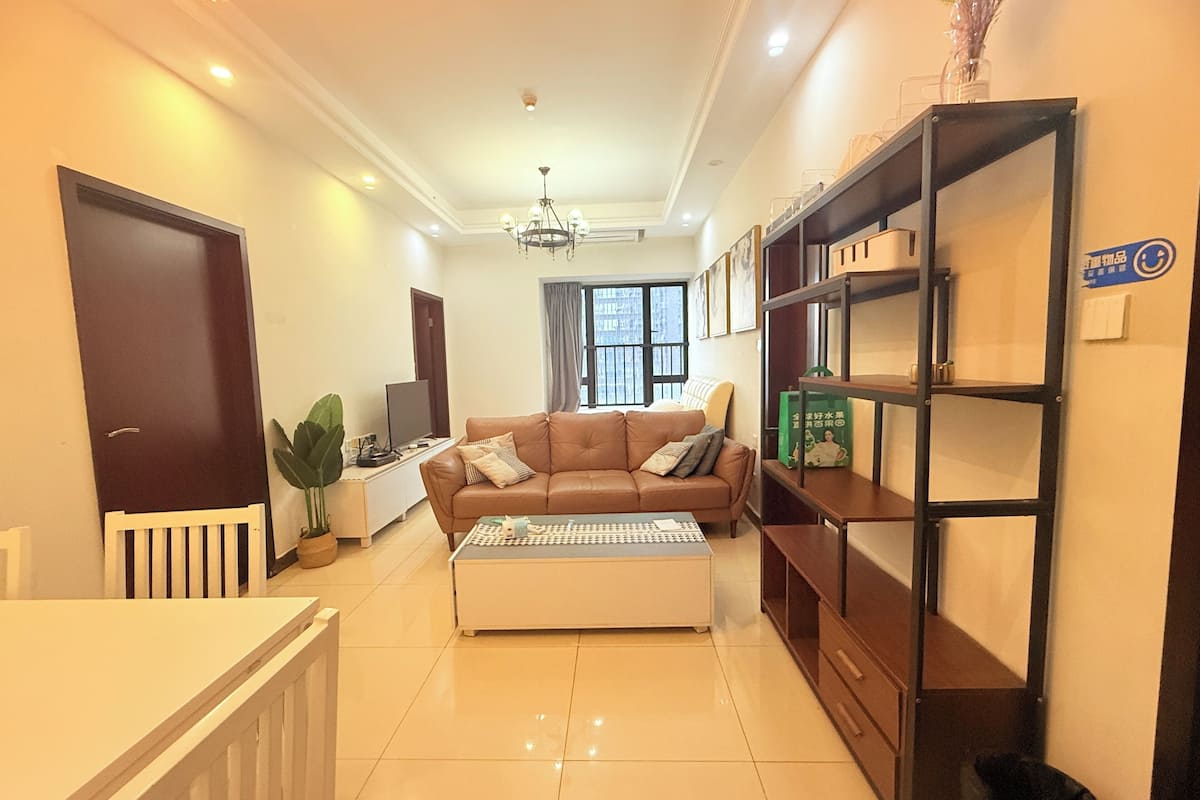 A living room with a sofa, a coffee table, a TV, a bookshelf, and a plant.