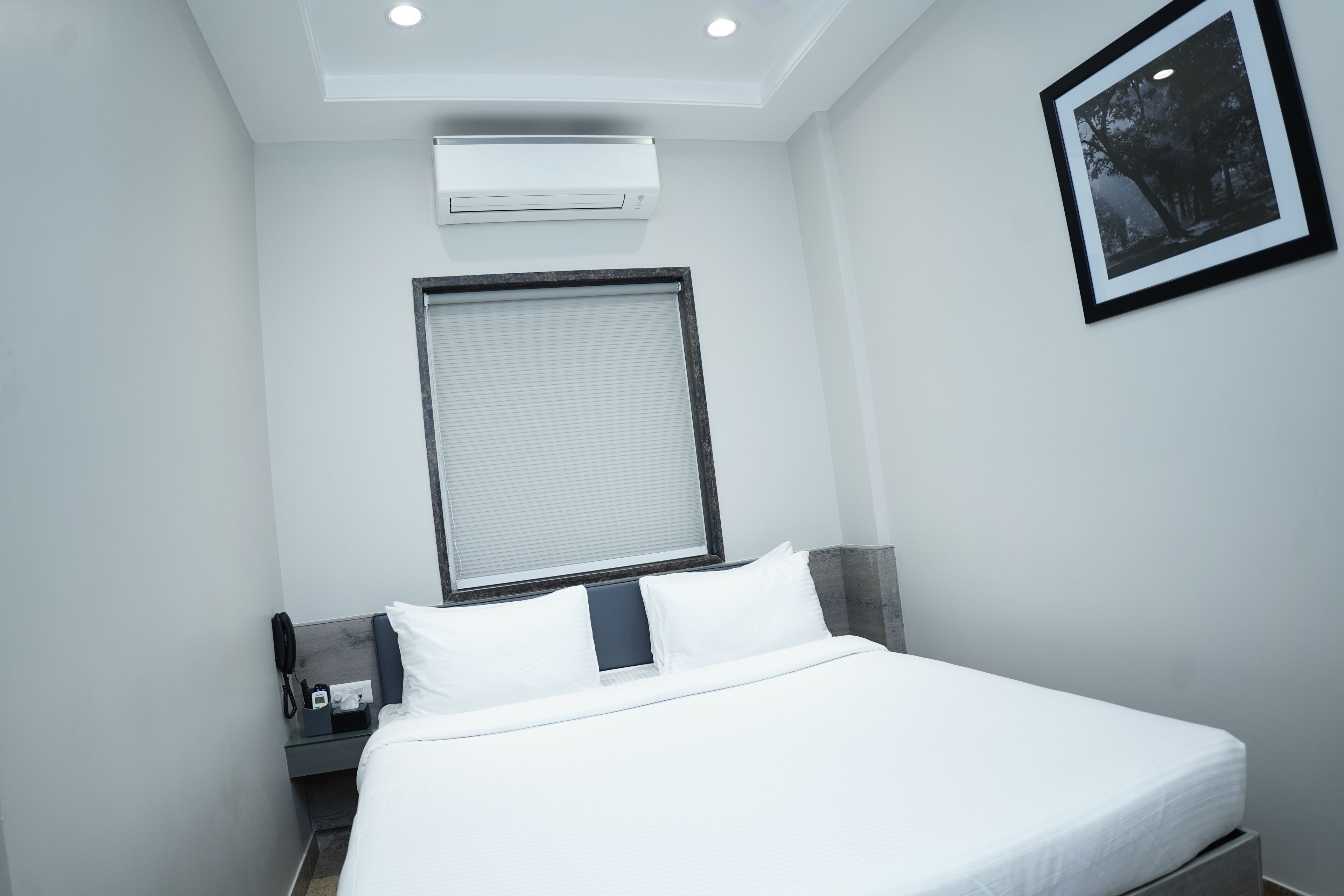 Quarto de hotel moderno com uma cama, mesa de cabeceira, ar condicionado, quadro na parede e janela com persianas.