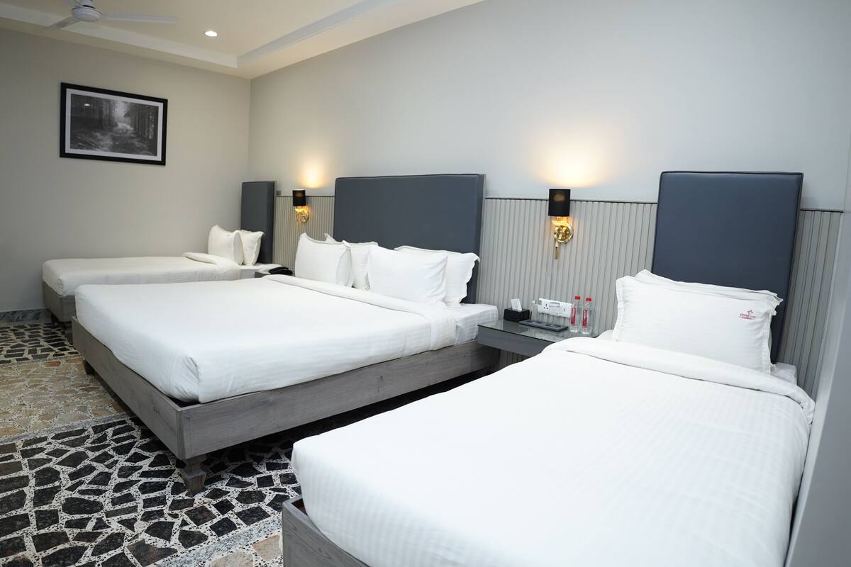 Ein Hotelzimmer mit drei Betten, einem Deckenventilator, einem gerahmten Bild an der Wand und Nachttischlampen.