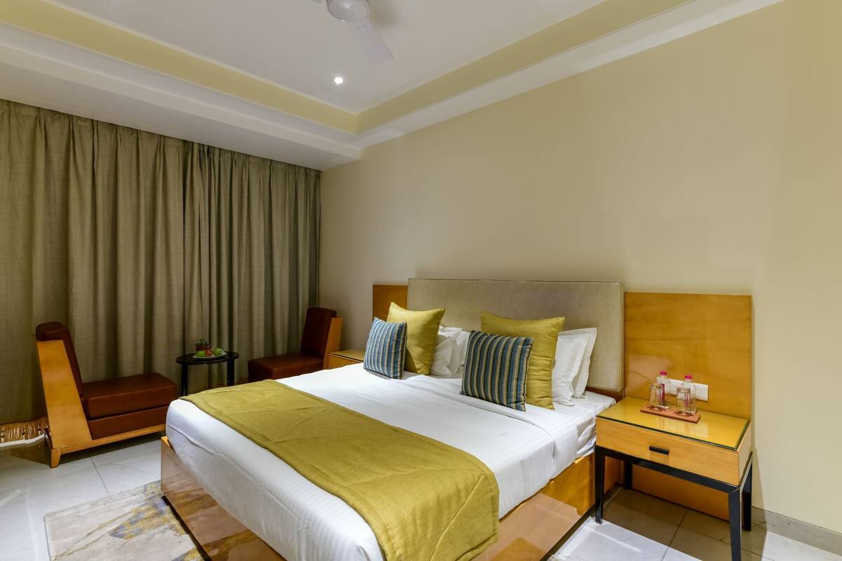 Ein Hotelzimmer mit einem großen Bett, einem Holfnachtschränkchen, einem Sessel und einem kleinen Tisch mit einer Pflanze.