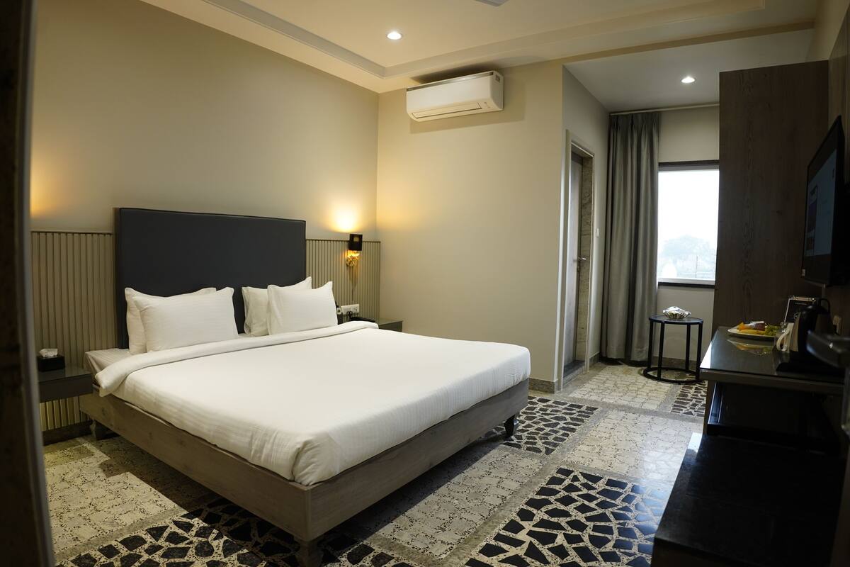 Ein Hotelzimmer mit einem großen Bett, einem Flachbildfernseher, einem kleinen Tisch mit Lampe und einem Fenster mit Vorhängen.