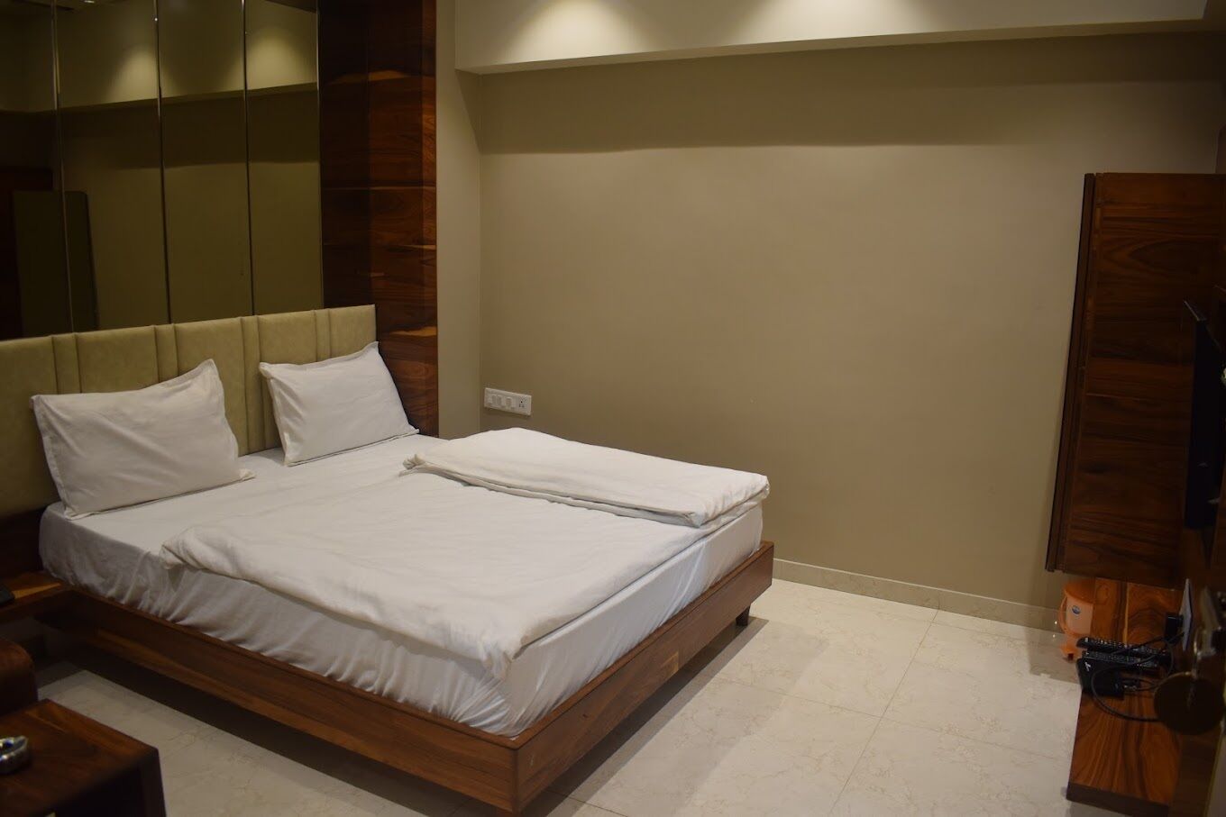 Een netjes opgemaakt bed in een kamer met een houten hoofdeinde, een houten kledingkast en een spiegel aan de muur.