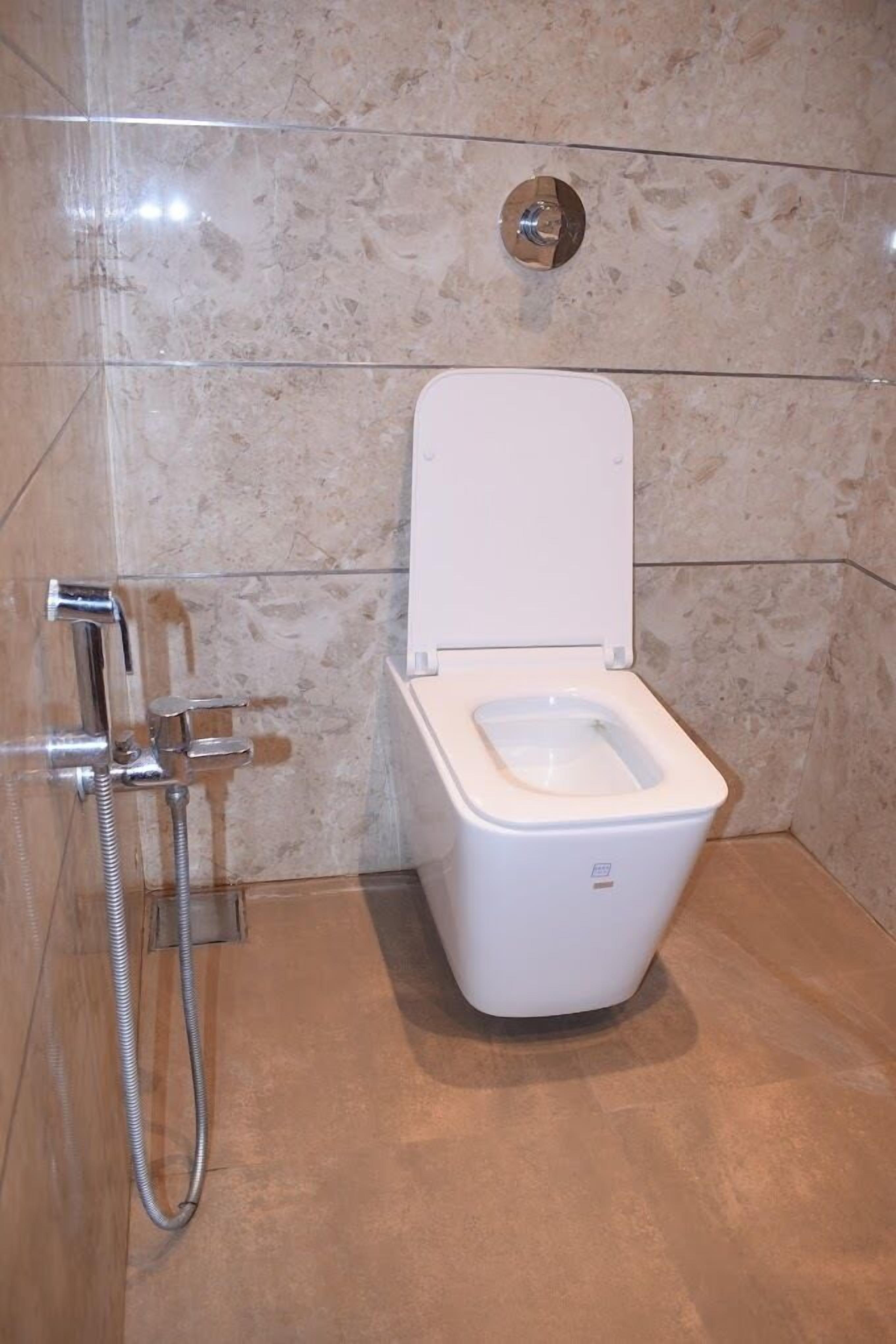 Un baño moderno con inodoro blanco, cabina de ducha y pared de mármol.