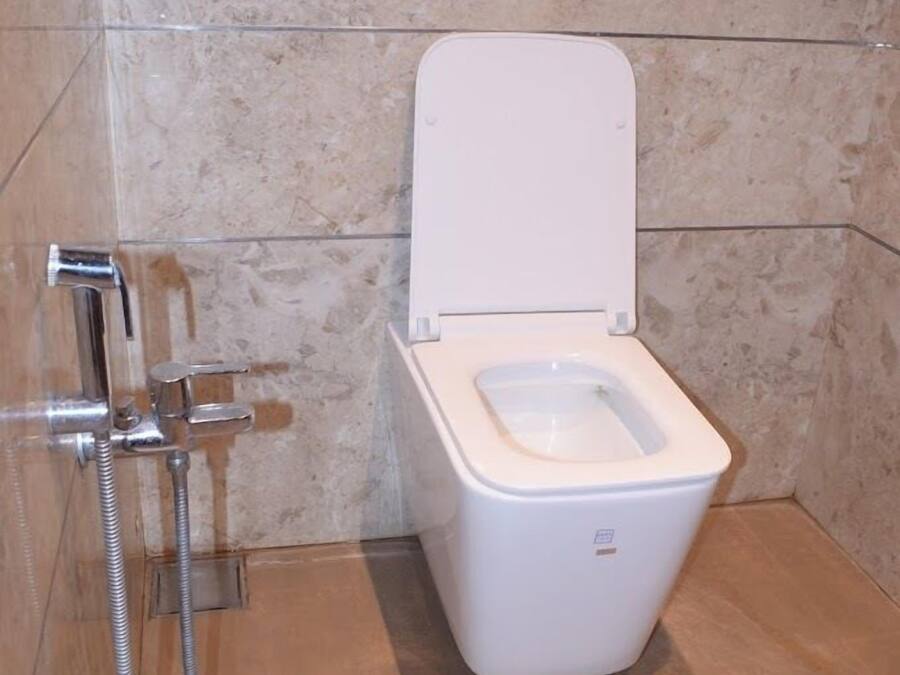 Un baño moderno con inodoro blanco, cabina de ducha y pared de mármol.