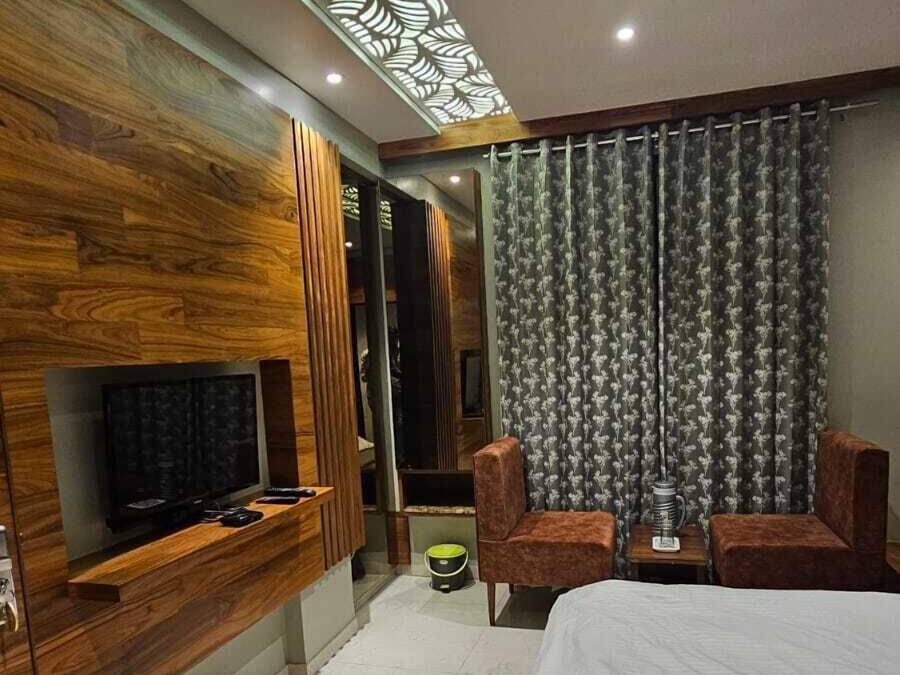 A modern bedroom with a bed, a TV, a seating area, and a patterned ceiling light.