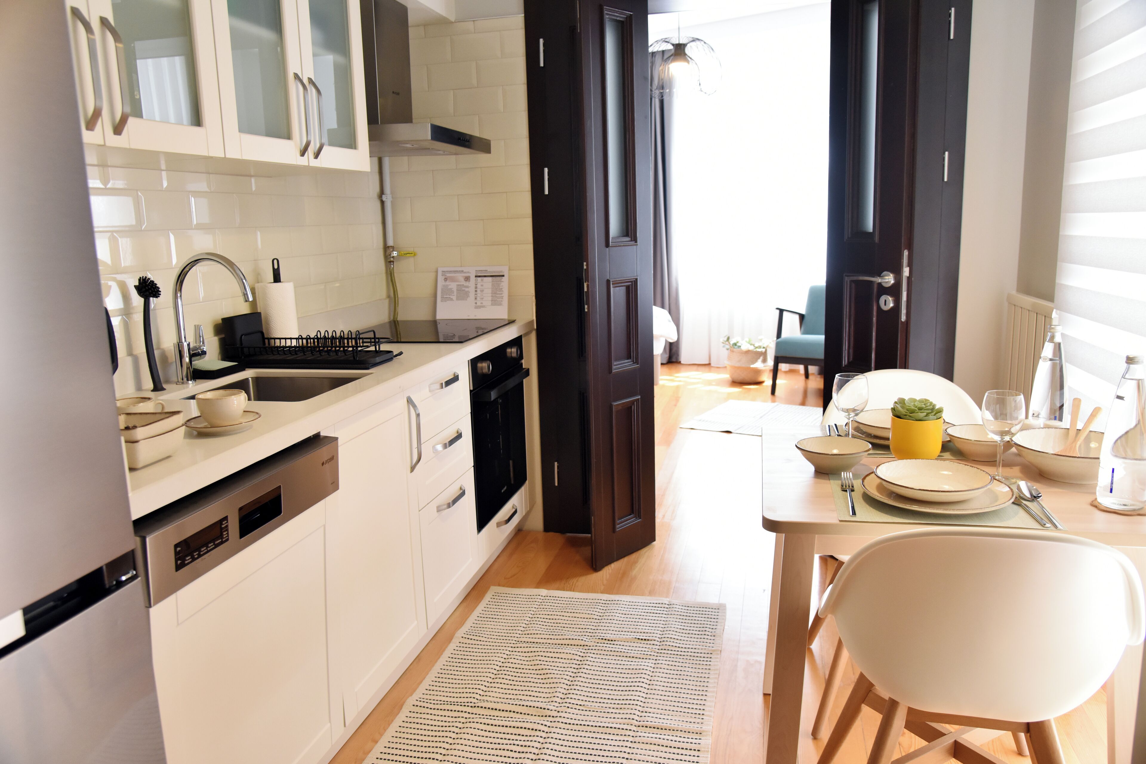 Una cocina moderna con armarios blancos, lavavajillas y un comedor con mesa preparada para dos.