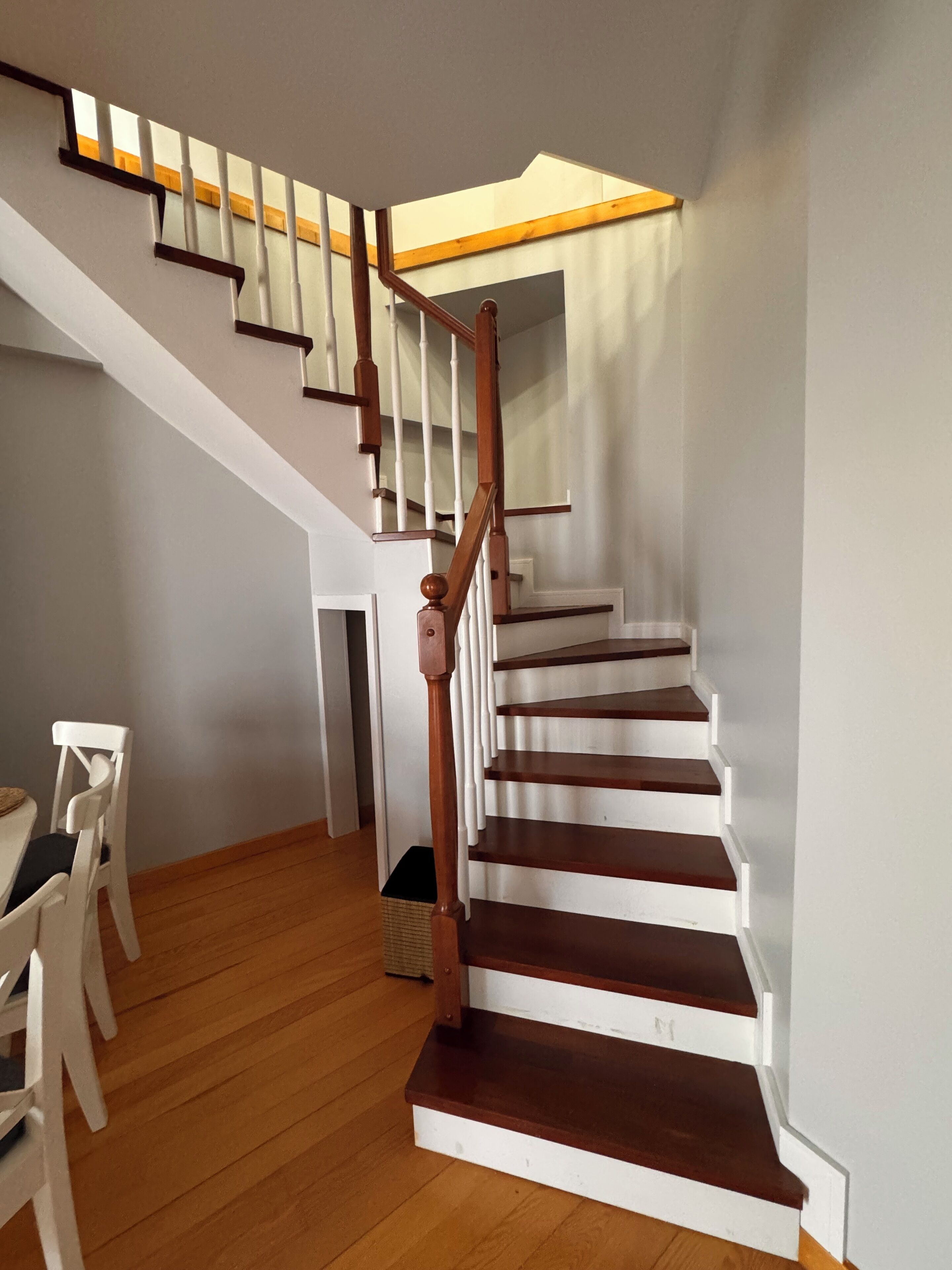 A staircase with wooden steps and white railings, leading to a landing with a wooden ceiling.