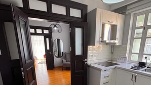 A modern kitchen with white cabinets, a wooden floor, and a large window. - İstanbul Guesthouse (Istanbul)