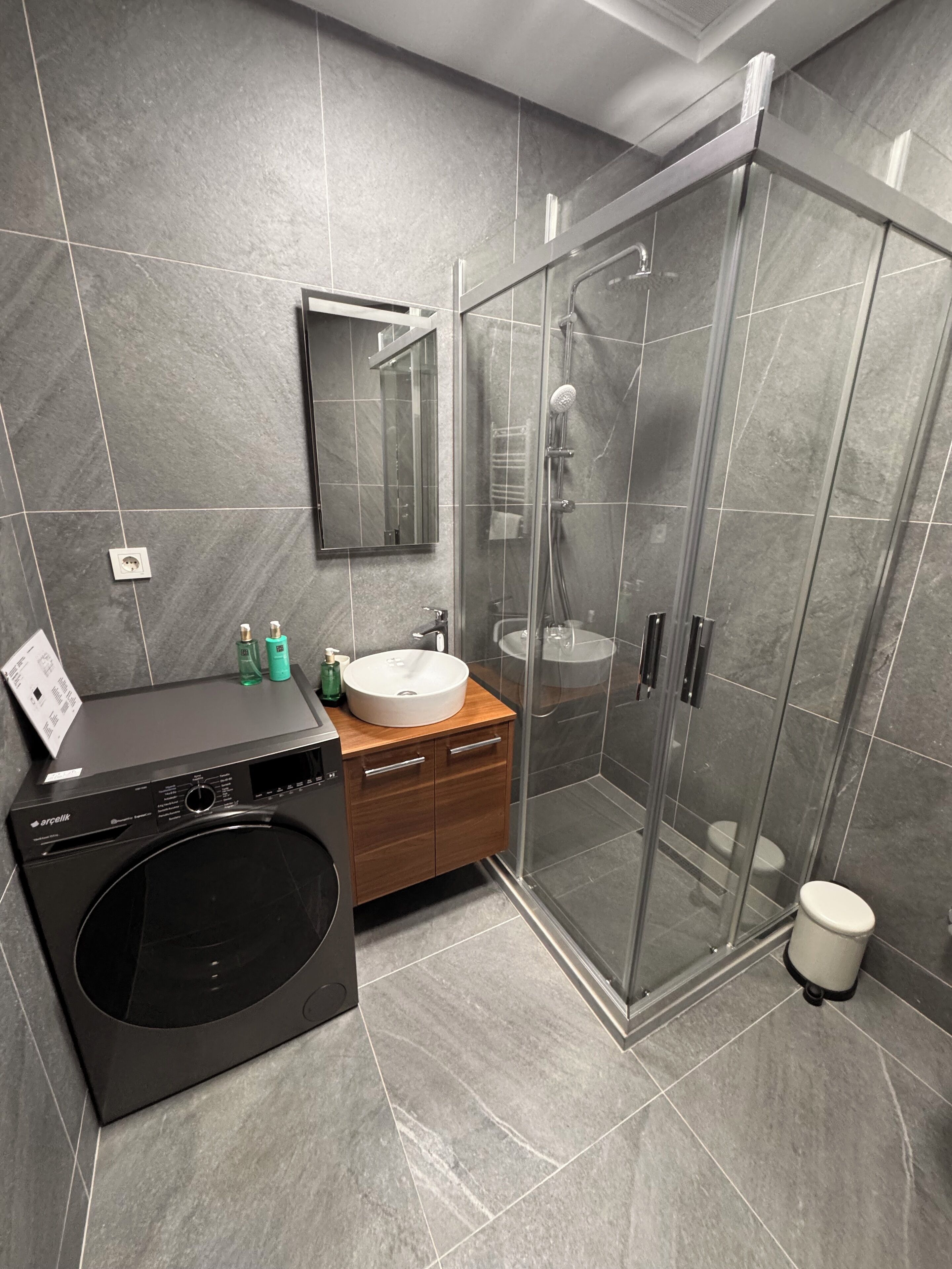 Une salle de bain moderne dotée d’une douche à parois de verre, d’un lave-linge encastré et d’un meuble-lavabo en bois.