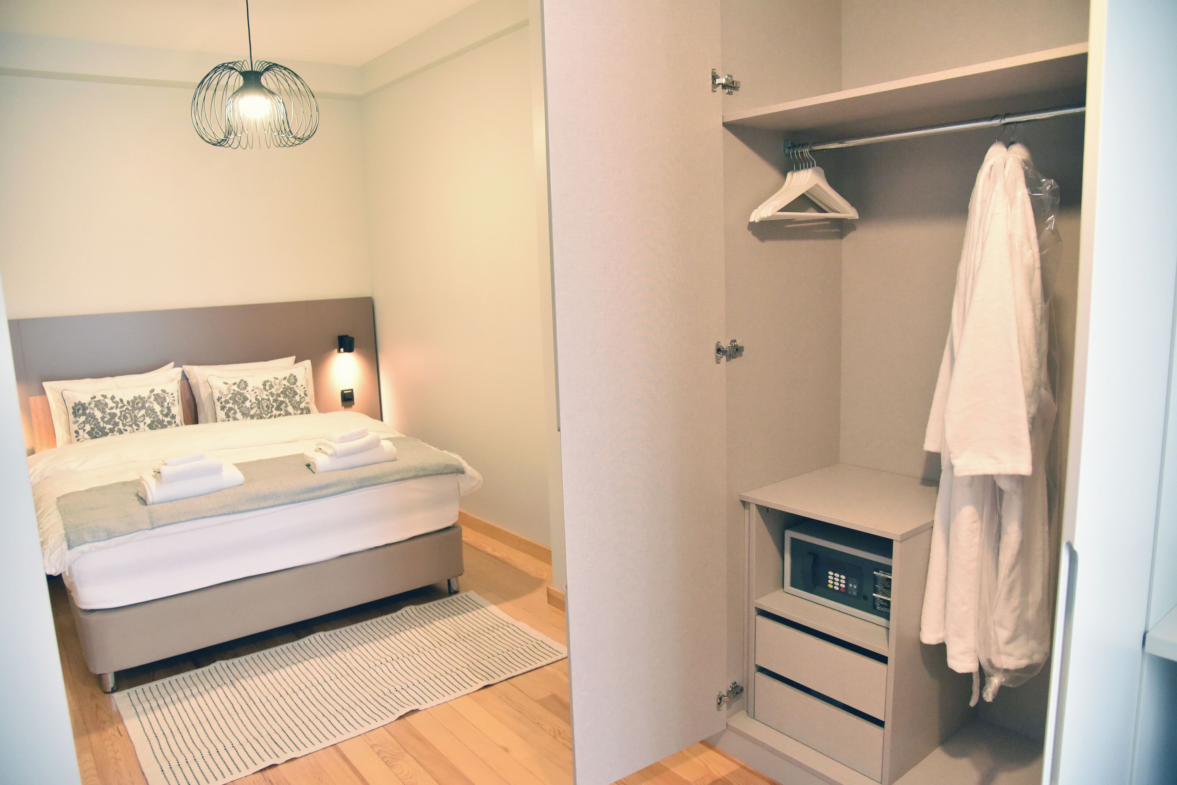 A bedroom with a bed, bedside lamp, and a walk-in closet with a hanging rack and a towel rack.
