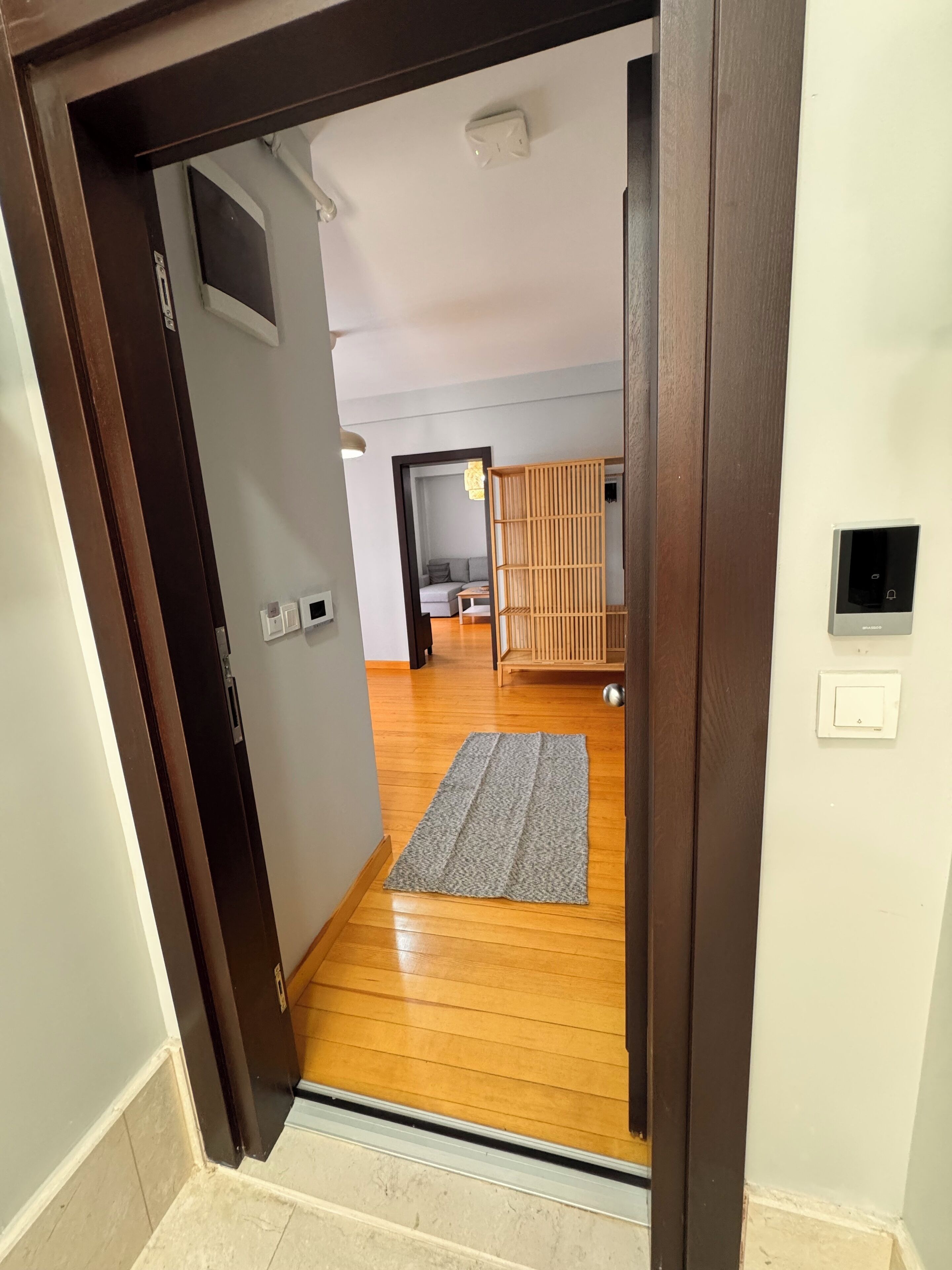 A doorway leading into a room with a wooden floor, a grey rug, a wooden partition, and a bed in the background.