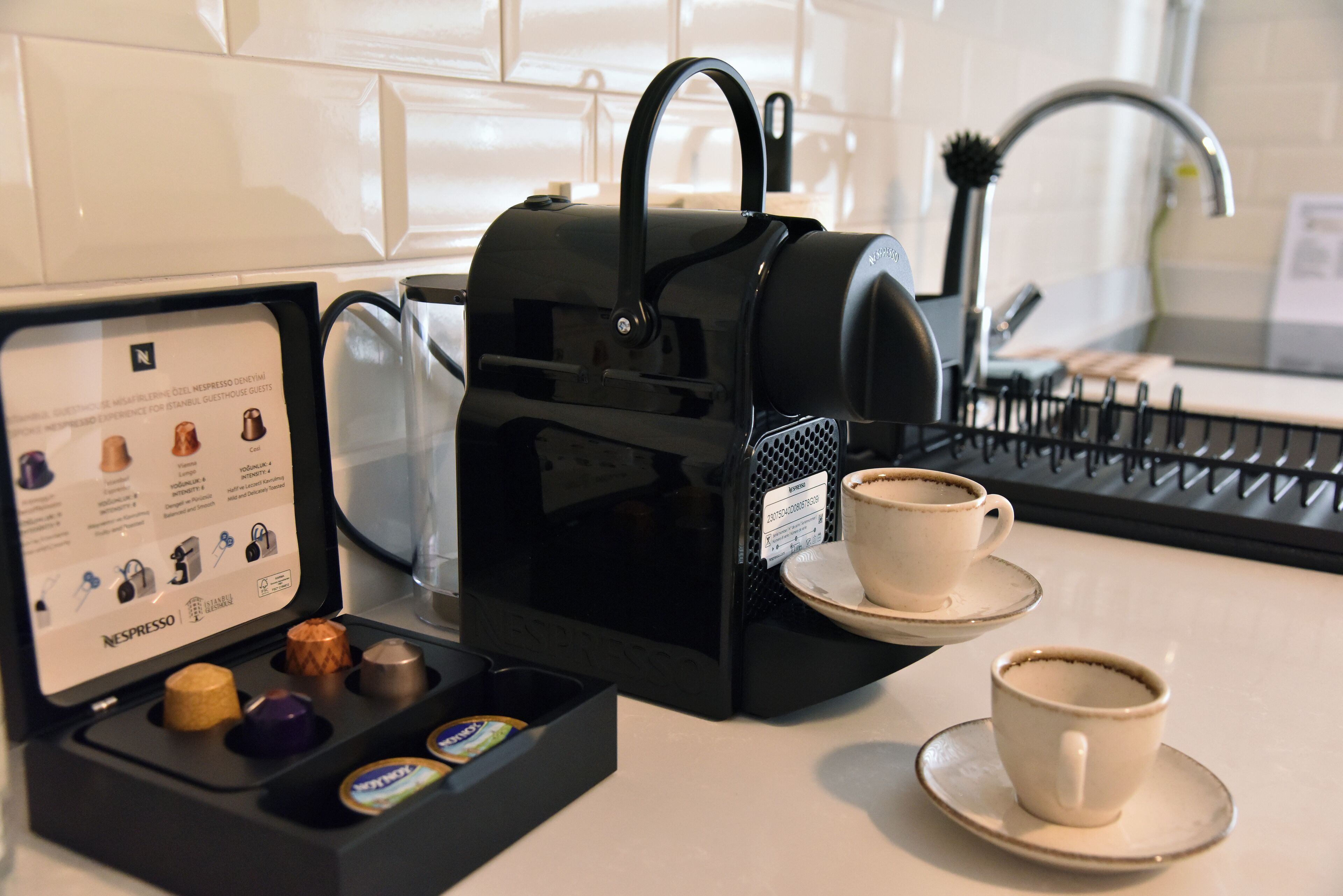 Une machine à café avec un présentoir de dosettes de café et deux tasses posées sur un comptoir de cuisine.