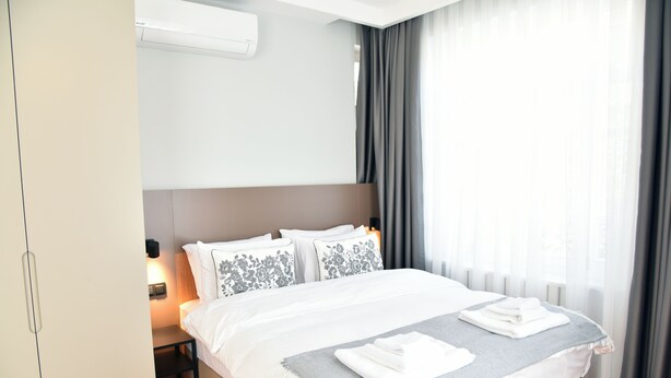 A hotel room with a large bed, a bedside table, an air conditioning unit, and a window with curtains. - İstanbul Guesthouse (Istanbul)