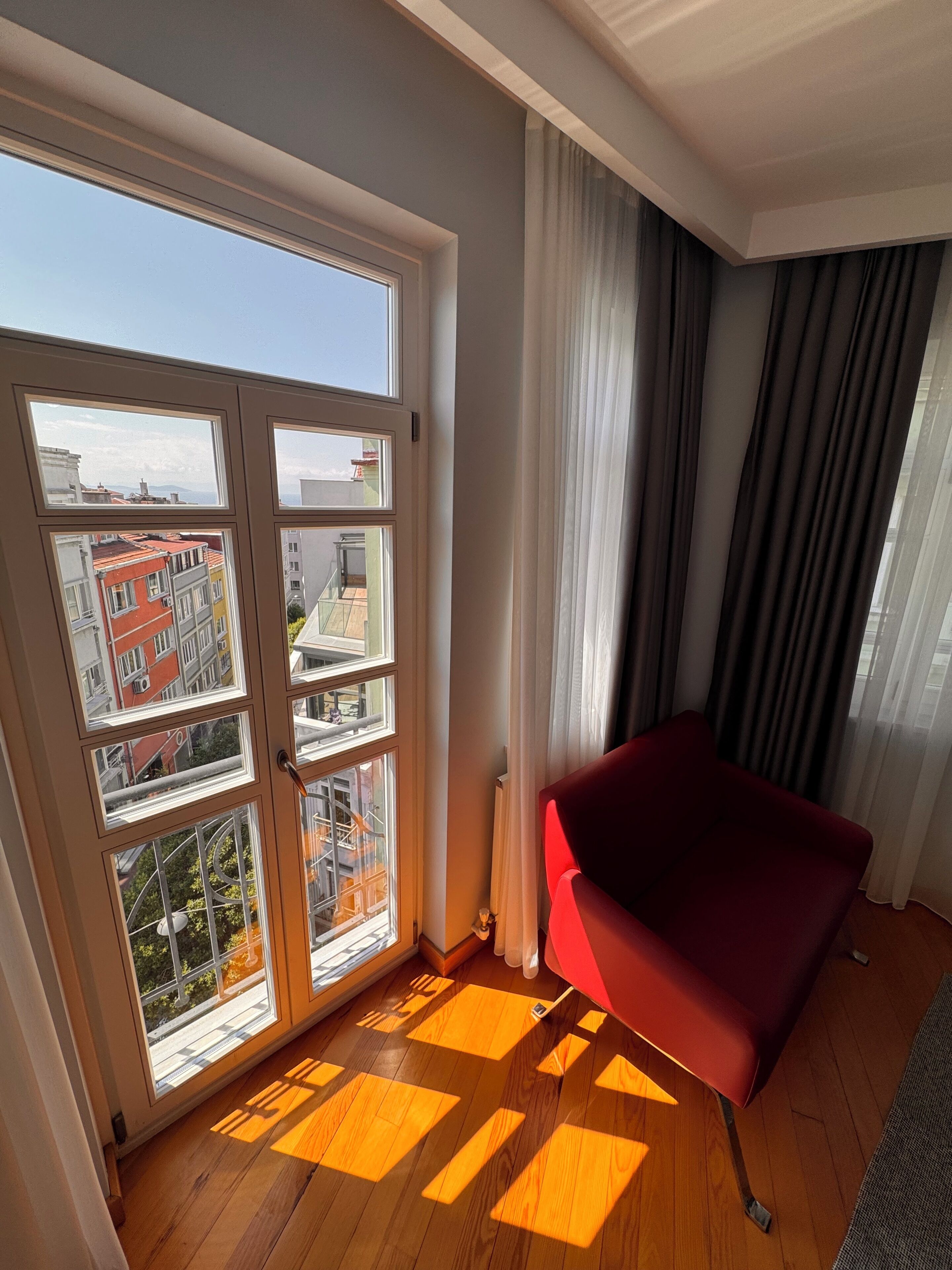 A room with a large sliding glass door leading to a balcony, a red sofa, and a wooden floor with geometric patterns.