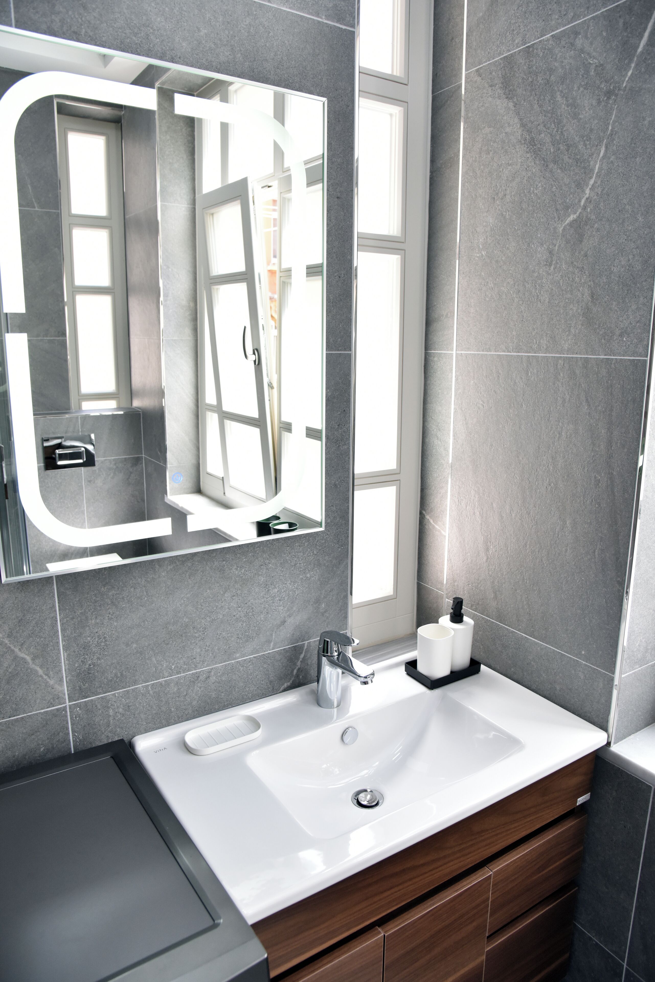 A modern bathroom with a large mirror, a white sink, and a wooden vanity.