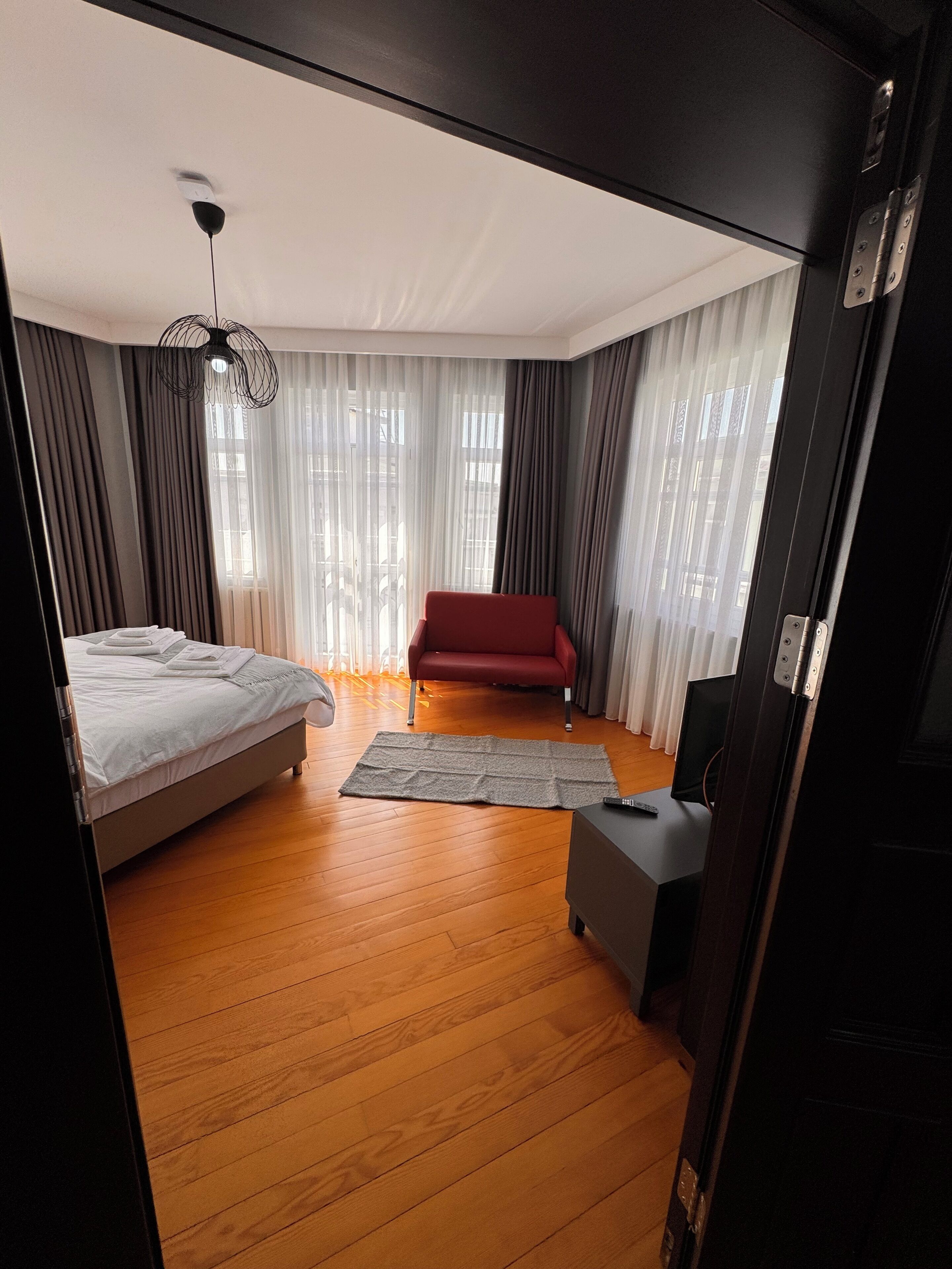 Une chambre d’hôtel moderne avec un lit, un canapé rouge, une petite table et un téléviseur.
