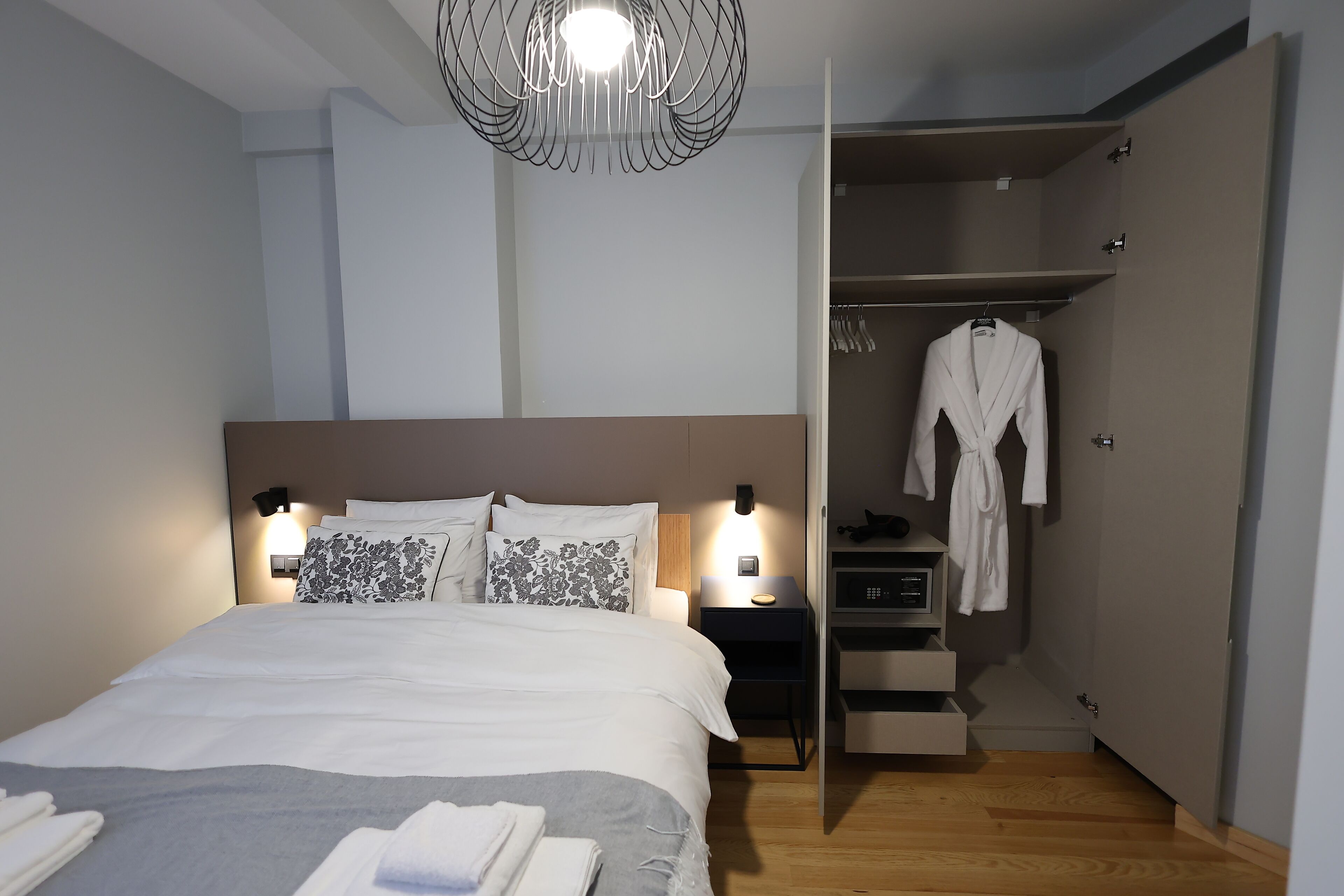 Una habitación de hotel moderna con una cama bien hecha, lámparas de noche, un vestidor y suelo de madera.