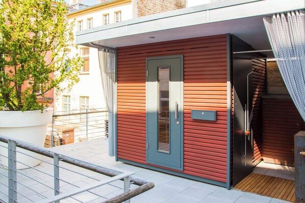 Un edificio moderno con fachada roja, una puerta gris y un pequeño balcón con barandilla metálica.