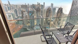 A balcony with two chairs and a table, overlooking a cityscape with high-rise buildings and a body of water.