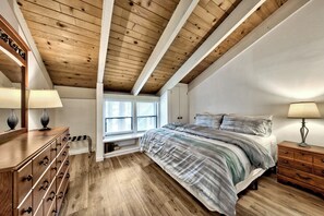 Ein Schlafzimmer mit Holzboden, einem Bett mit gestreifter Bettdecke, einem Schminktisch und einem Nachttischchen mit Lampe.