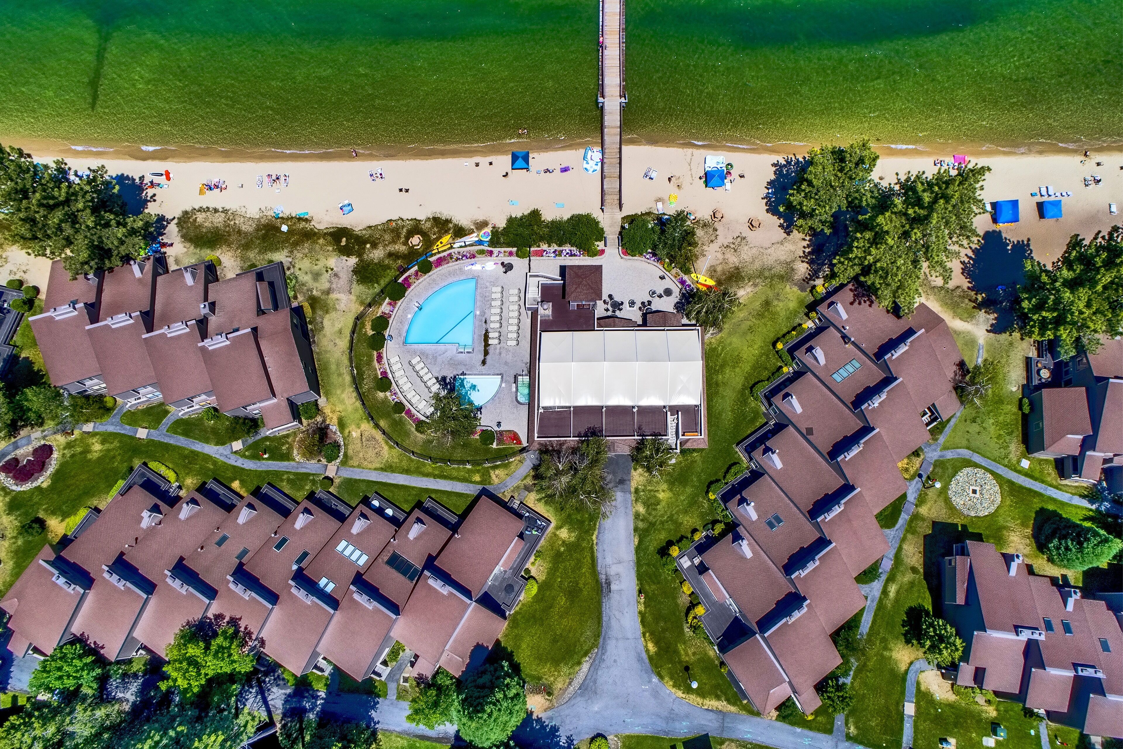 An aerial view of a residential area with a swimming pool, beach, and multiple houses.