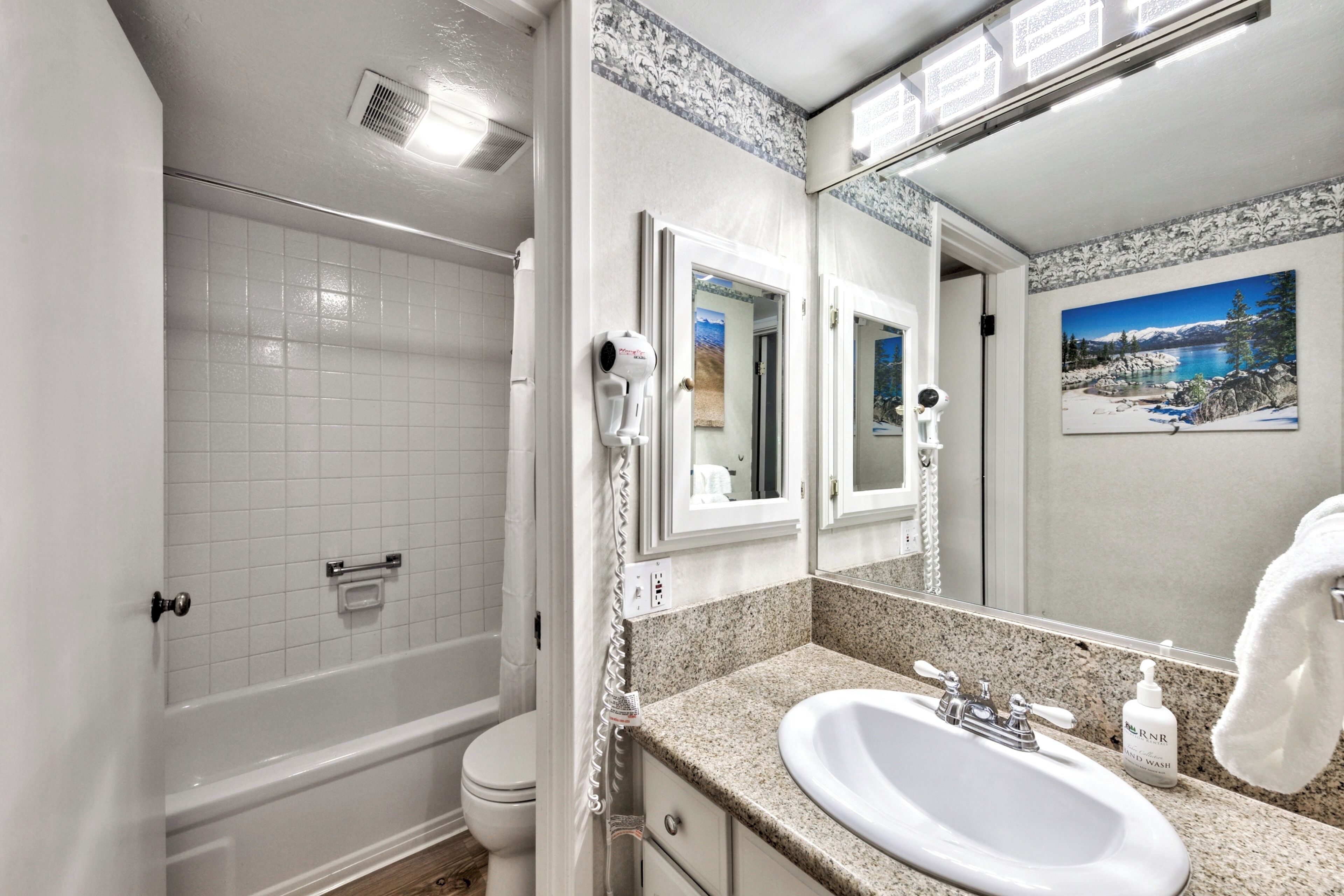 Un baño con lavamanos blanco, espejo, toalla y ducha.