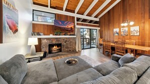 A cozy living room with a stone fireplace, a large sofa, and a dining area with wooden furniture.