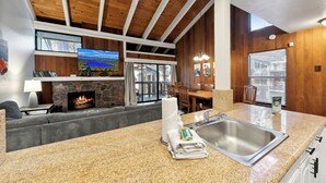A modern kitchen with granite countertops, a stone fireplace, and a dining area with wooden furniture.