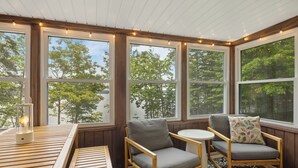 Une véranda avec de grandes fenêtres, une table en bois, deux chaises et une lanterne.
