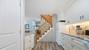 Une cuisine moderne avec des meubles blancs, un escalier en bois et un plan de travail en granit.