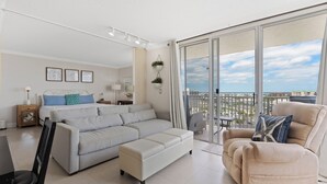 Una sala de estar moderna con sofá, reposapiés y sillón, una mesa de comedor y un balcón con vistas a la ciudad.