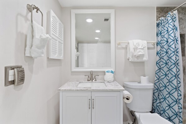 Un baño con lavamanos blanco, espejo, inodoro y cortina de ducha.